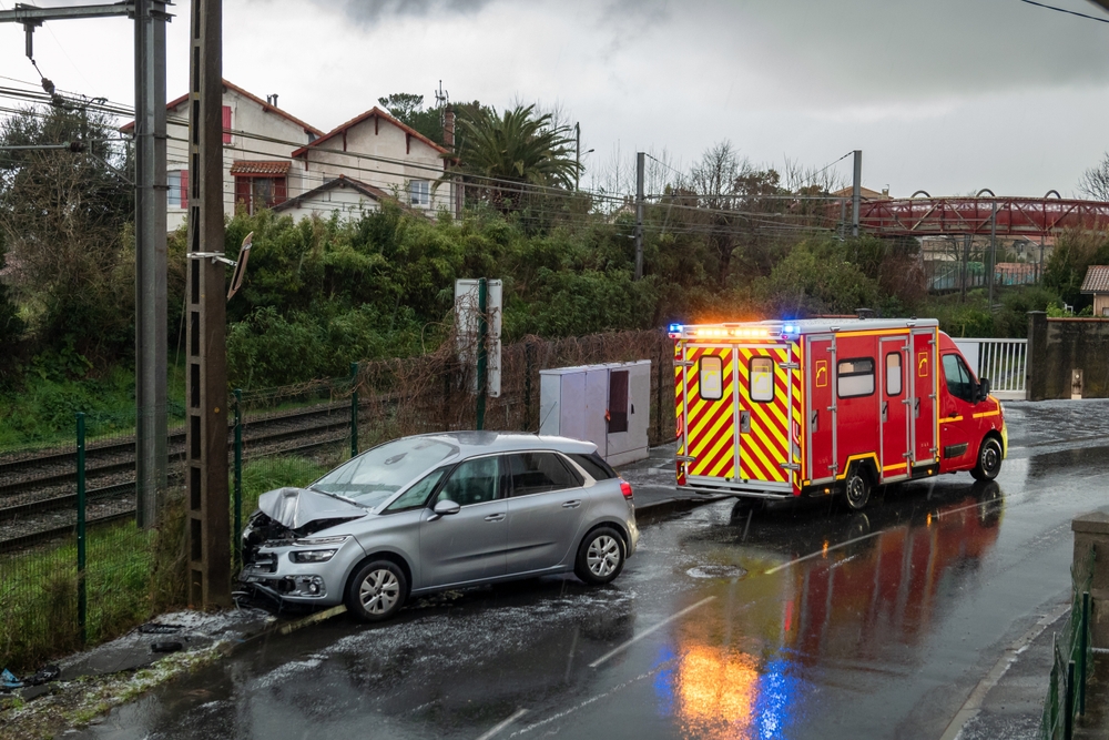 Silver car crashed into a utility pole with an ambulance on scene after a rainy road accident
