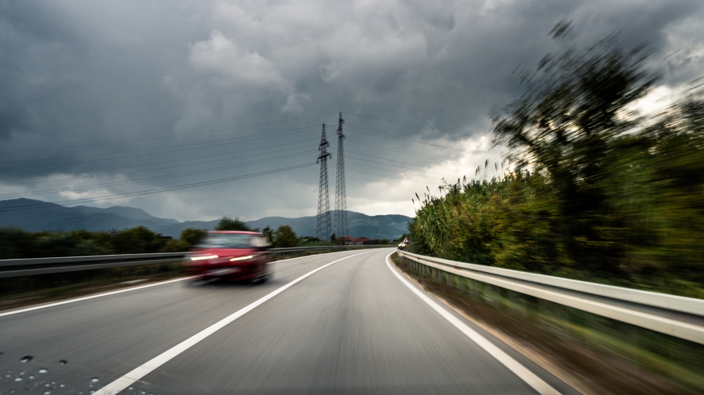 Red car speeding on a highway under cloudy skies, representing reckless driving.