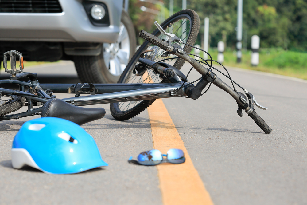 bicycle lying in the middle of the road after a crash next to a car and a blue helmet