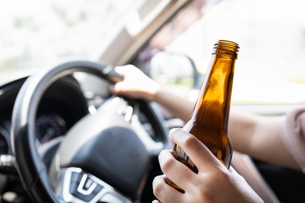 Driver holding a beer bottle behind the wheel, illustrating evidence of drunk driving