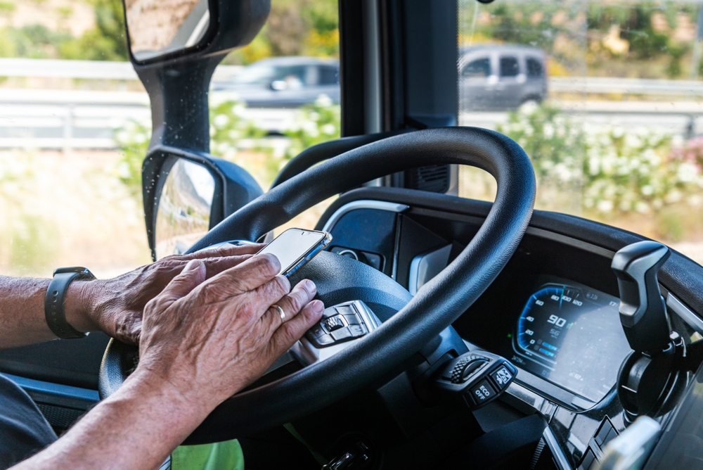 Commercial driver using a cell phone while driving, illustrating distracted driving risks on Massachusetts roadways.