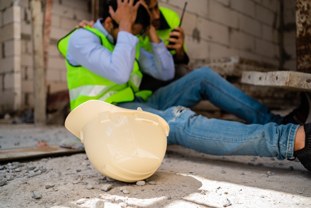 Construction worker sitting on the ground holding his head after a workplace accident, representing head injuries at Massachusetts construction sites
