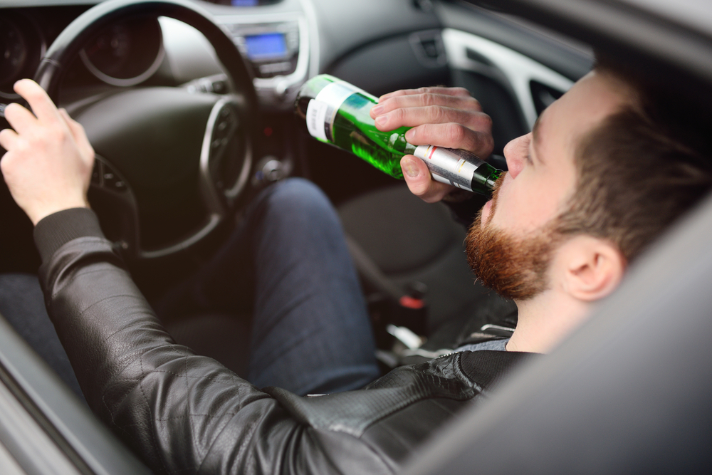 Driver holding an open bottle of alcohol while seated behind the wheel of a car