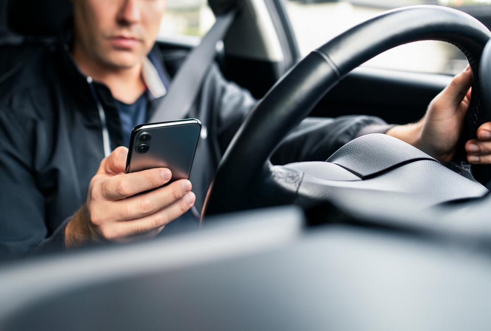 Rideshare driver checking his phone app while seated in the driver's seat after an accident