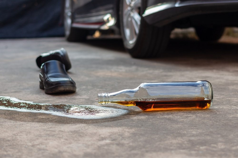 Spilled liquor bottle and a man's shoe lying on the pavement near a car after a drunk driving accident